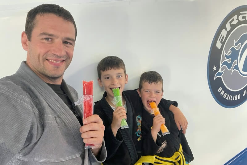 Een lesgever en twee jongens in kimono eten een ijspegel na de training.